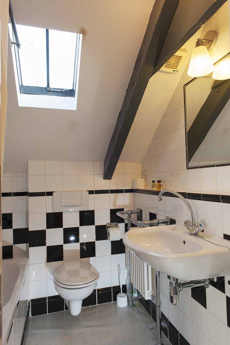 Small Bathroom. Checked black and white tiles on the wall. Large mirror, sink. Toilet. Bath.
